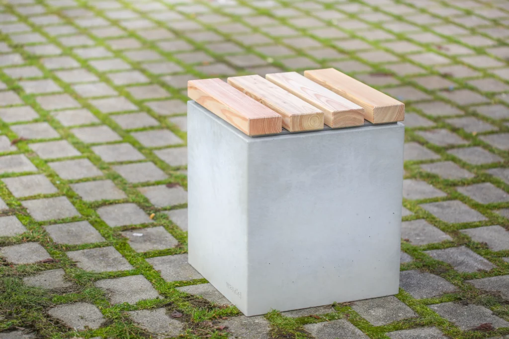 Hocker aus Beton mit Sitzauflage aus Lärchenholz steht auf öffentlicher Grünanlage
