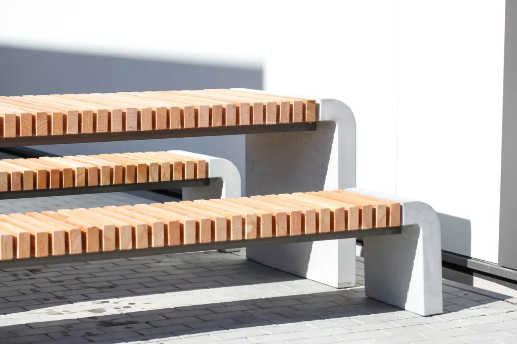 Sitzgruppe mit Tischfußen und Bankfüßen aus Sichtbeton, Auflagen aus längs verlaufenden Holzdielen, steht auf öffentlichem Grund