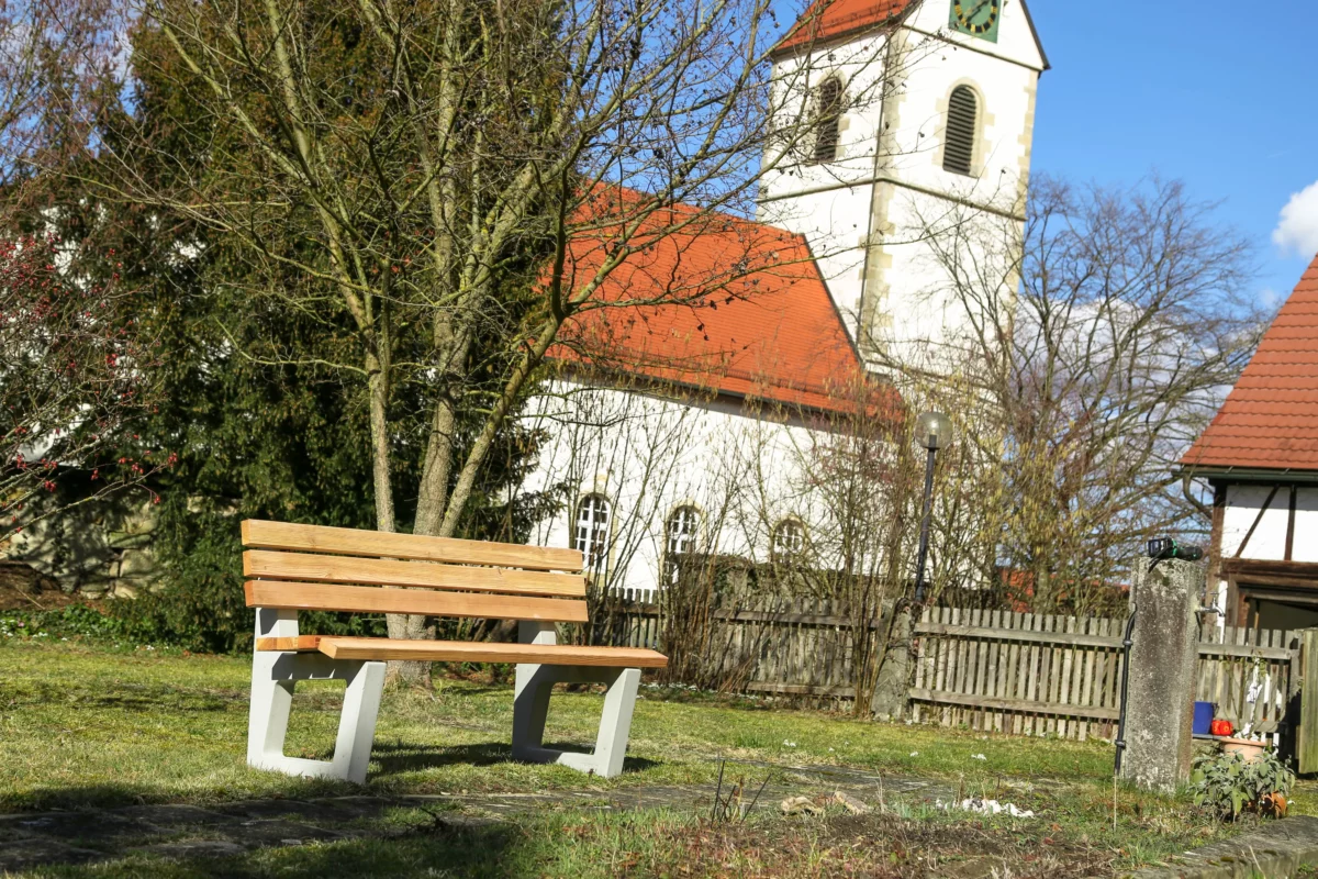 Ergonomische Sitzbank mit Lärchenholzlatten und Füßen aus Beton steht an einem öffentlichen Weg