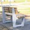 Ergonomische Sitzbank mit Lärchenholzlatten und Füßen aus Beton steht an einem öffentlichen Weg