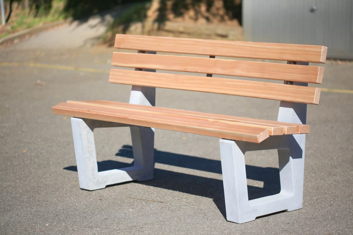 Ergonomische Sitzbank mit Lärchenholzlatten und Füßen aus Beton steht an einem öffentlichen Weg