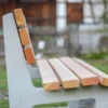 Ergonomische Sitzbank mit Lärchenholzlatten und Füßen aus Beton steht an einem öffentlichen Weg