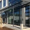 Ascher Kubus steht vor einem modernen Firmengebäude mit großer Glasfront