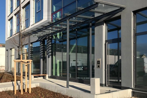 Ascher Kubus steht vor einem modernen Firmengebäude mit großer Glasfront
