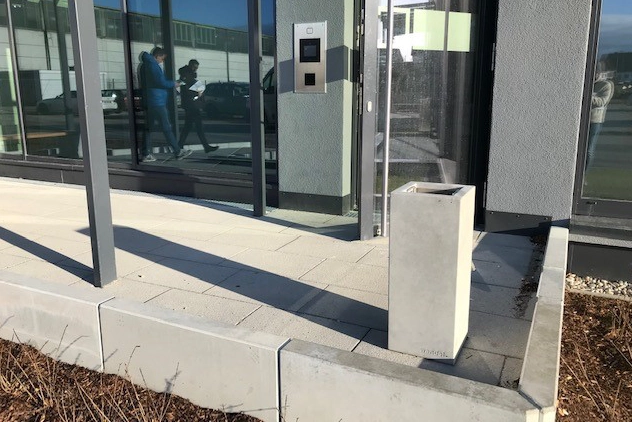 Ascher Kubus steht vor einem modernen Firmengebäude mit großer Glasfront