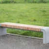 Moderne Sitzbank mit abgerundeten Füßen aus Beton und längs verlaufenden Holzlatten steht in einer öffentlichen Grünanlage.
