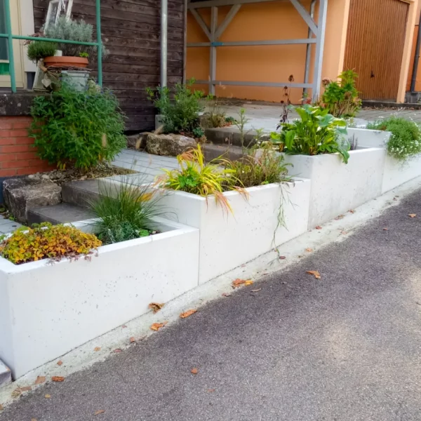 Pflanztröge aus Beton stehen schön bepflanzt als Abgrenzung zur Straße vor einem Privaten Haus.