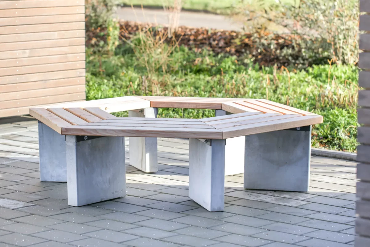 Rundbank mit Lärchenholzlatten, Rückenlehne und Betonfüßen steht auf einem öffentlichen Platz.