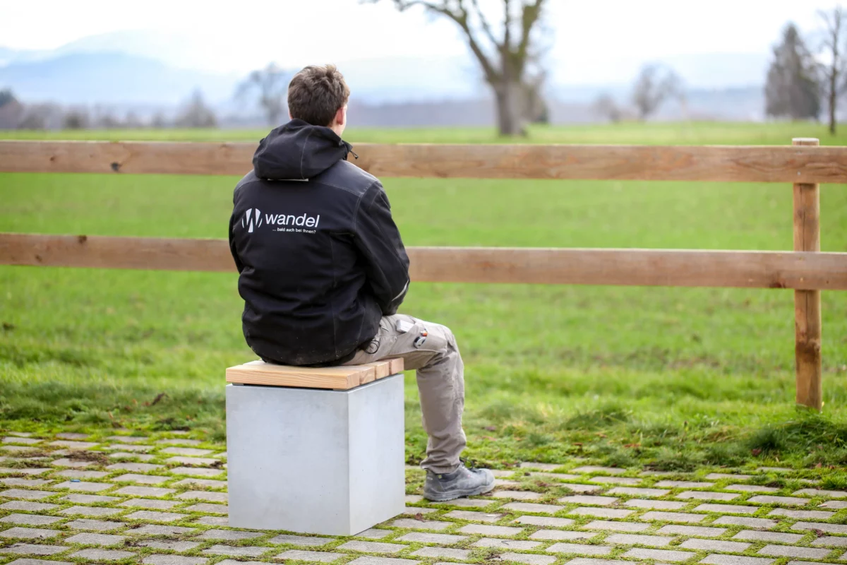 Hocker aus Beton mit Sitzauflage aus Lärchenholz steht auf öffentlicher Grünanlage