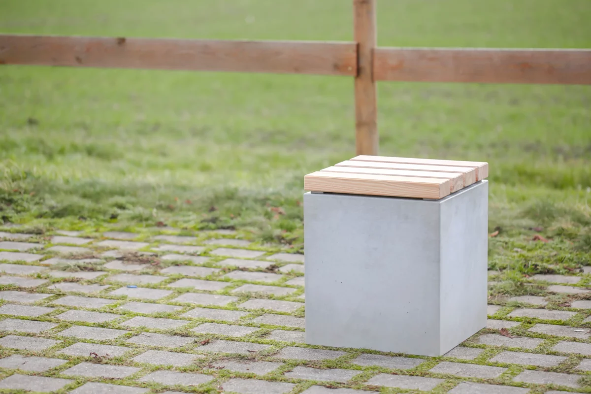 Hocker aus Beton mit Sitzauflage aus Lärchenholz steht auf öffentlicher Grünanlage