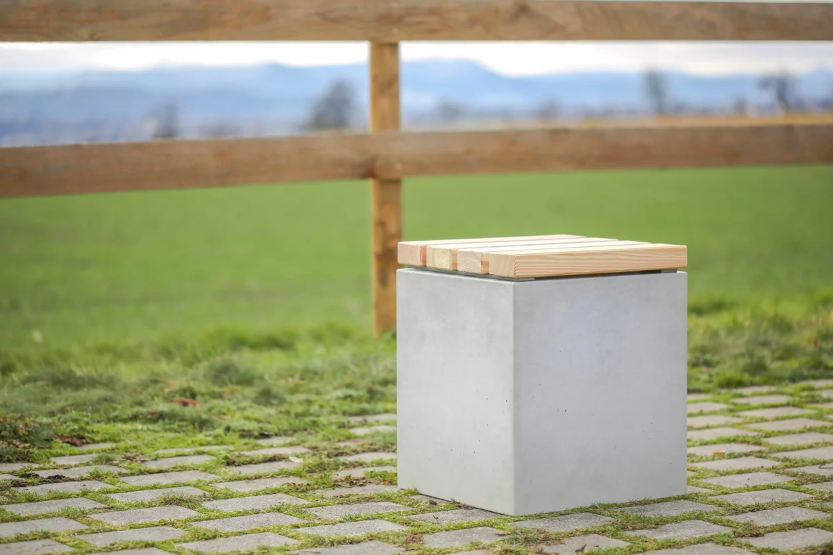 Hocker aus Beton mit Sitzauflage aus Lärchenholz steht auf öffentlicher Grünanlage