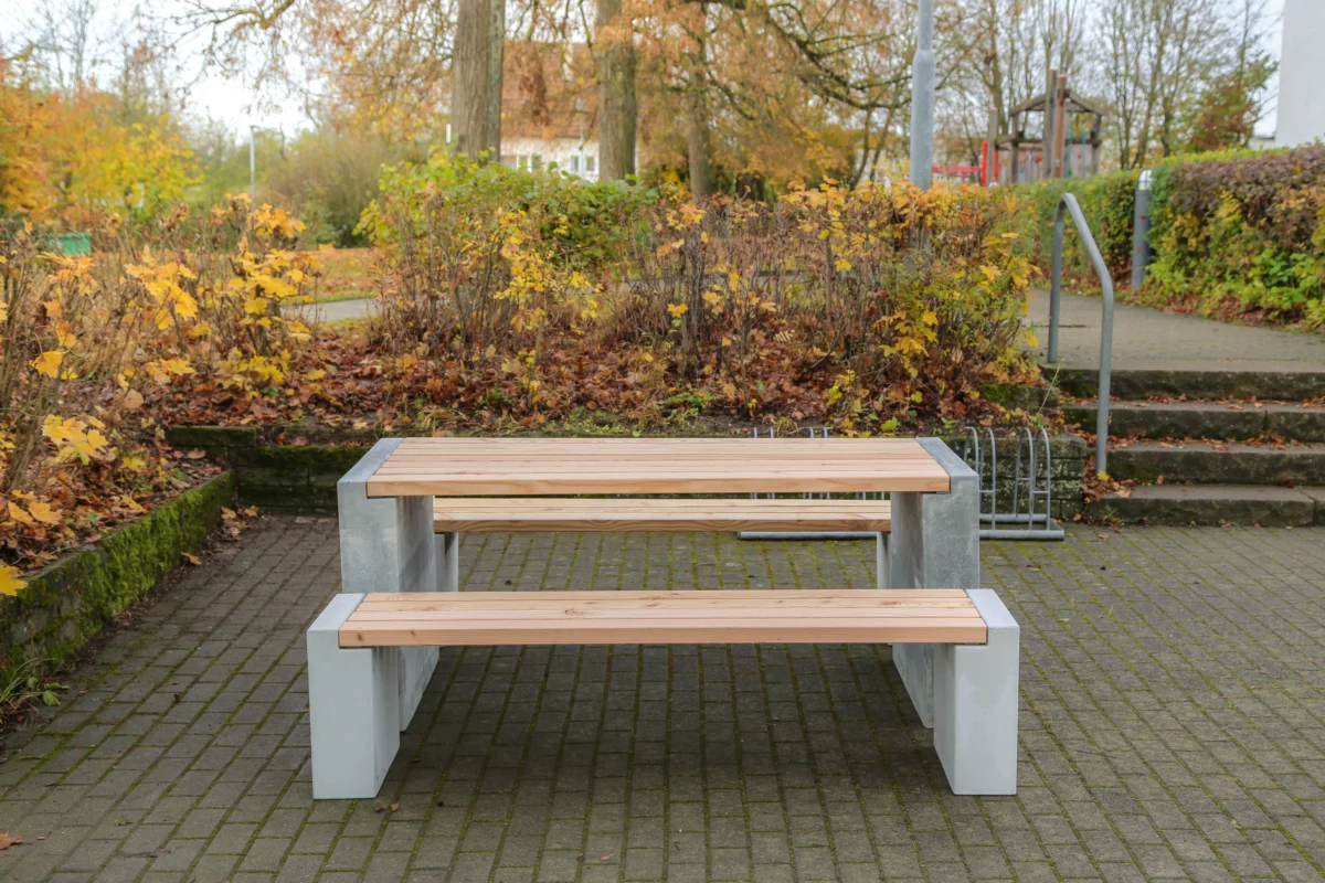 Sitzgruppe aus Sichtbeton und Lärchenholz steht in einem öffentlichen Park