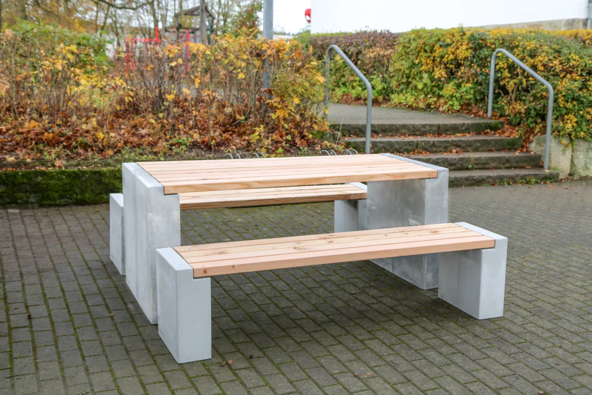 Sitzgruppe aus Sichtbeton und Lärchenholz steht in einem öffentlichen Park