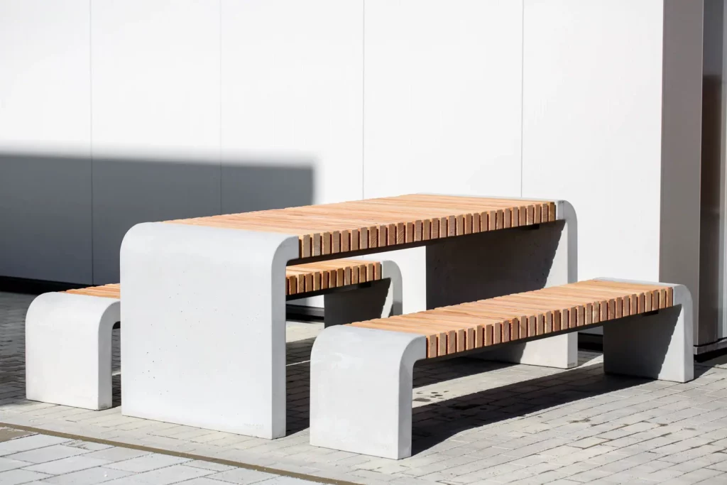 Tisch für Außenbereich mit abgerundeten Standfüßen aus Beton und längs verlaufenden Holzdielen steht auf öffentlichem Grund