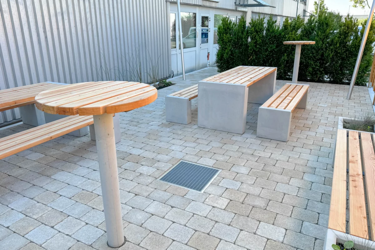 Stehtisch mit Betonfuß zum Einbetonieren und Auflage aus Lärchenholz steht in Mitarbeiterbereich eines Firmengeländes